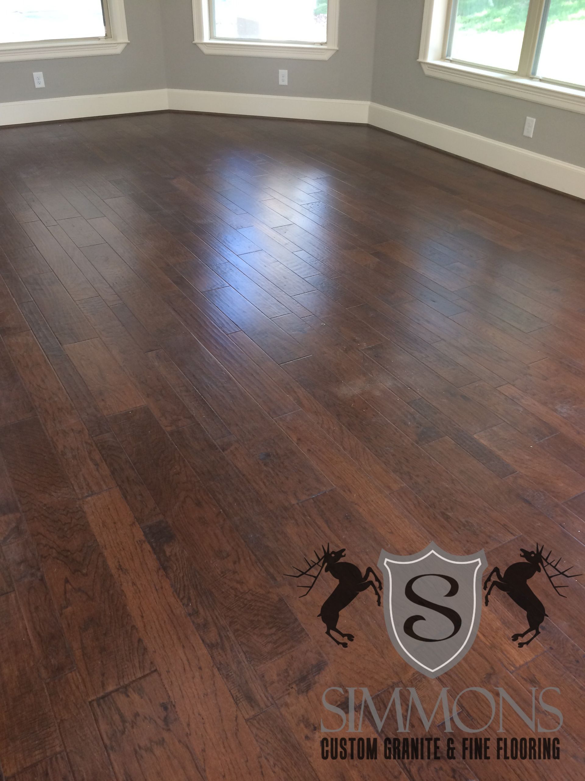 Empty room with dark hardwood floors, white walls, and three windows letting in daylight.