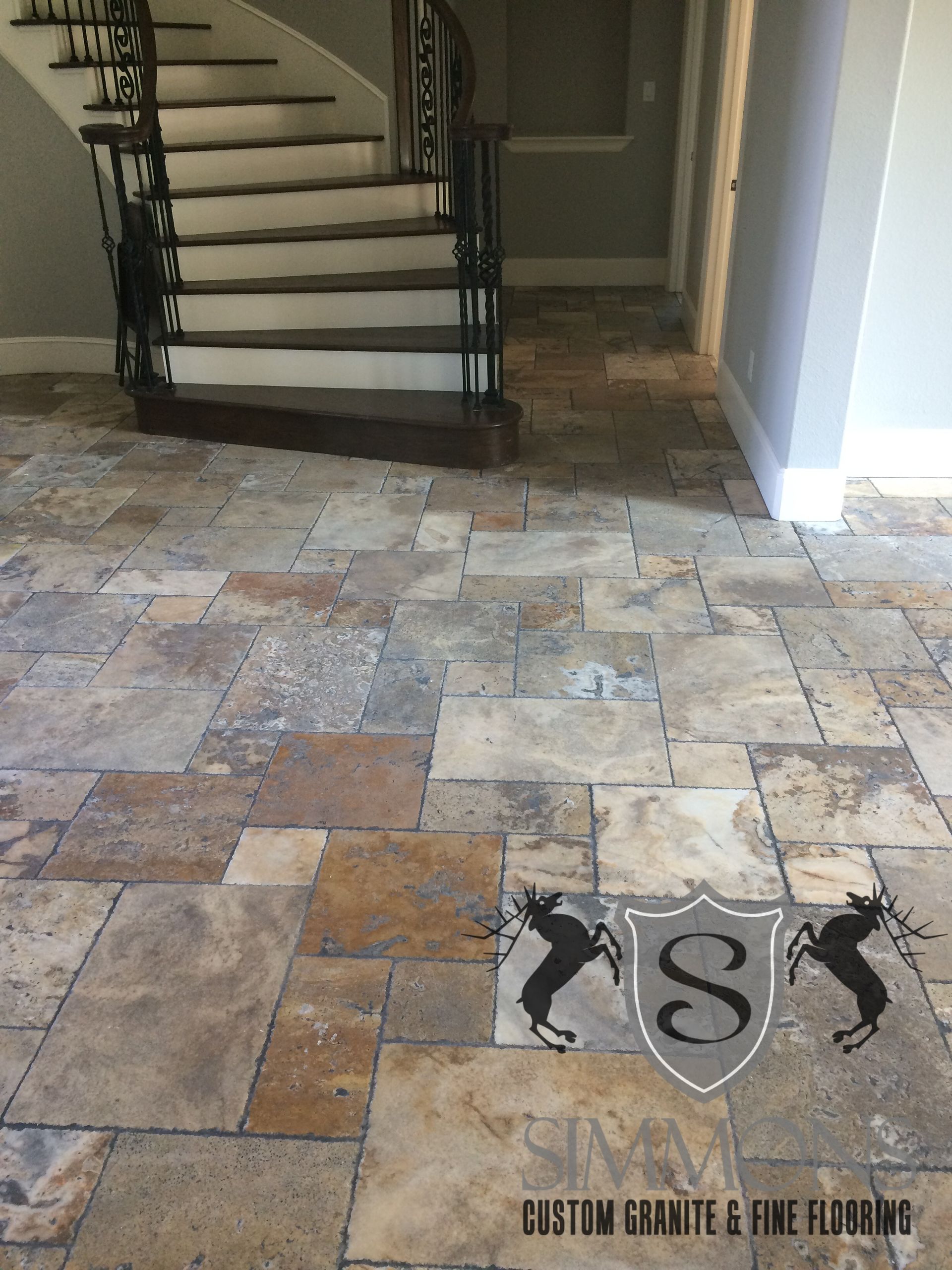 Stone-tile foyer with staircase and black wrought-iron railings leading to an upper floor.