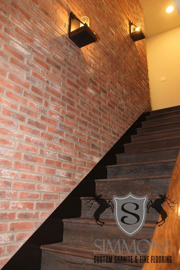 Brick-walled stairwell with dark wooden stairs and warm wall sconces leading upward