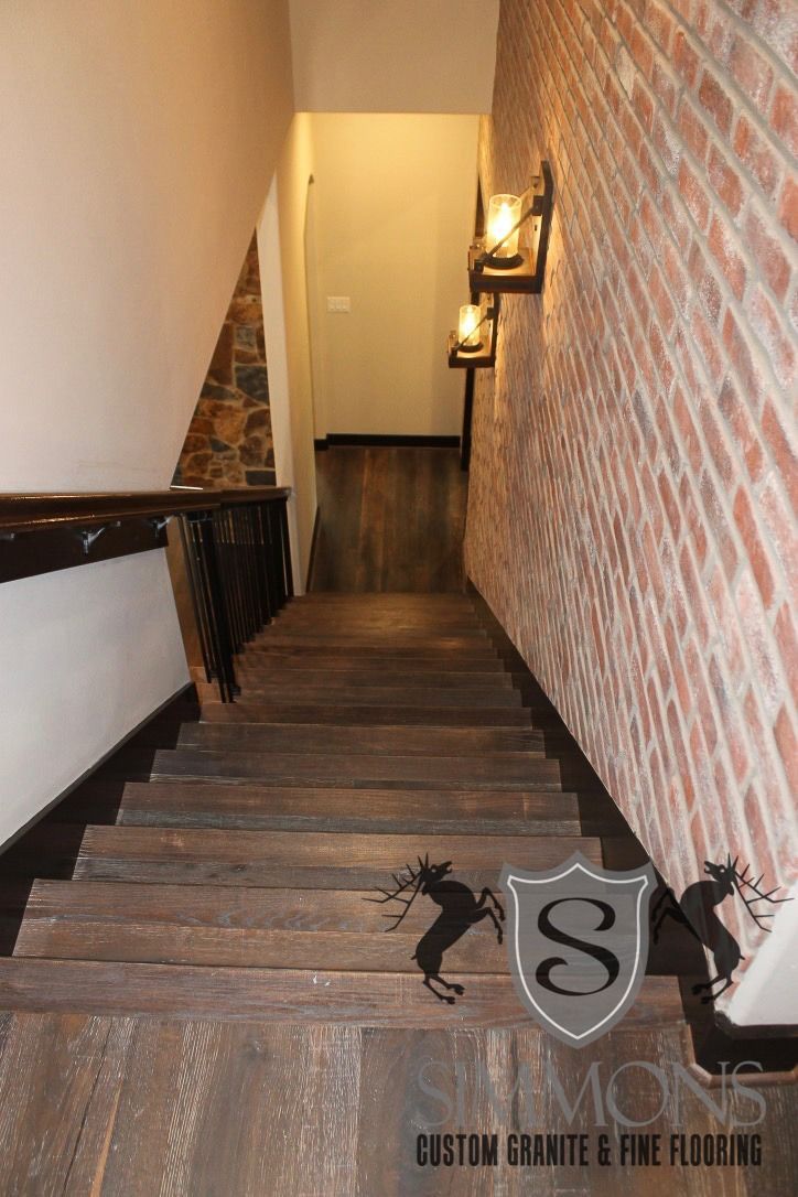 Narrow wooden staircase beside a brick wall with wall sconces leading to a hallway