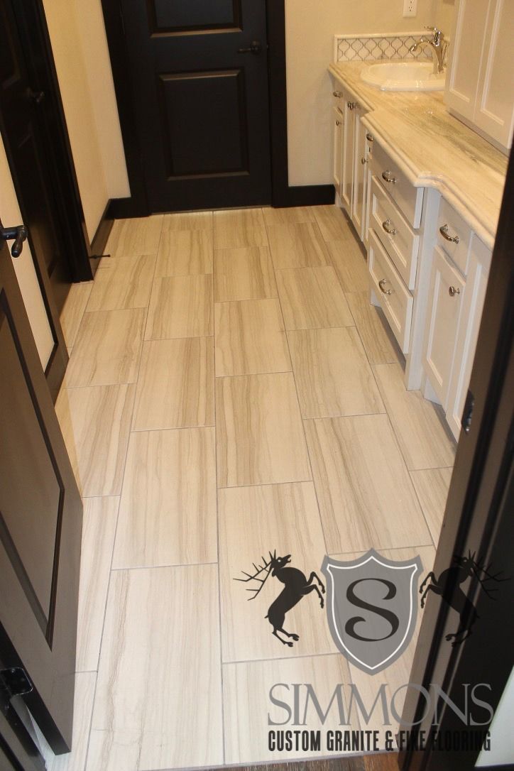 Narrow bathroom with beige tile floor, white cabinets, and a dark door at the far end.
