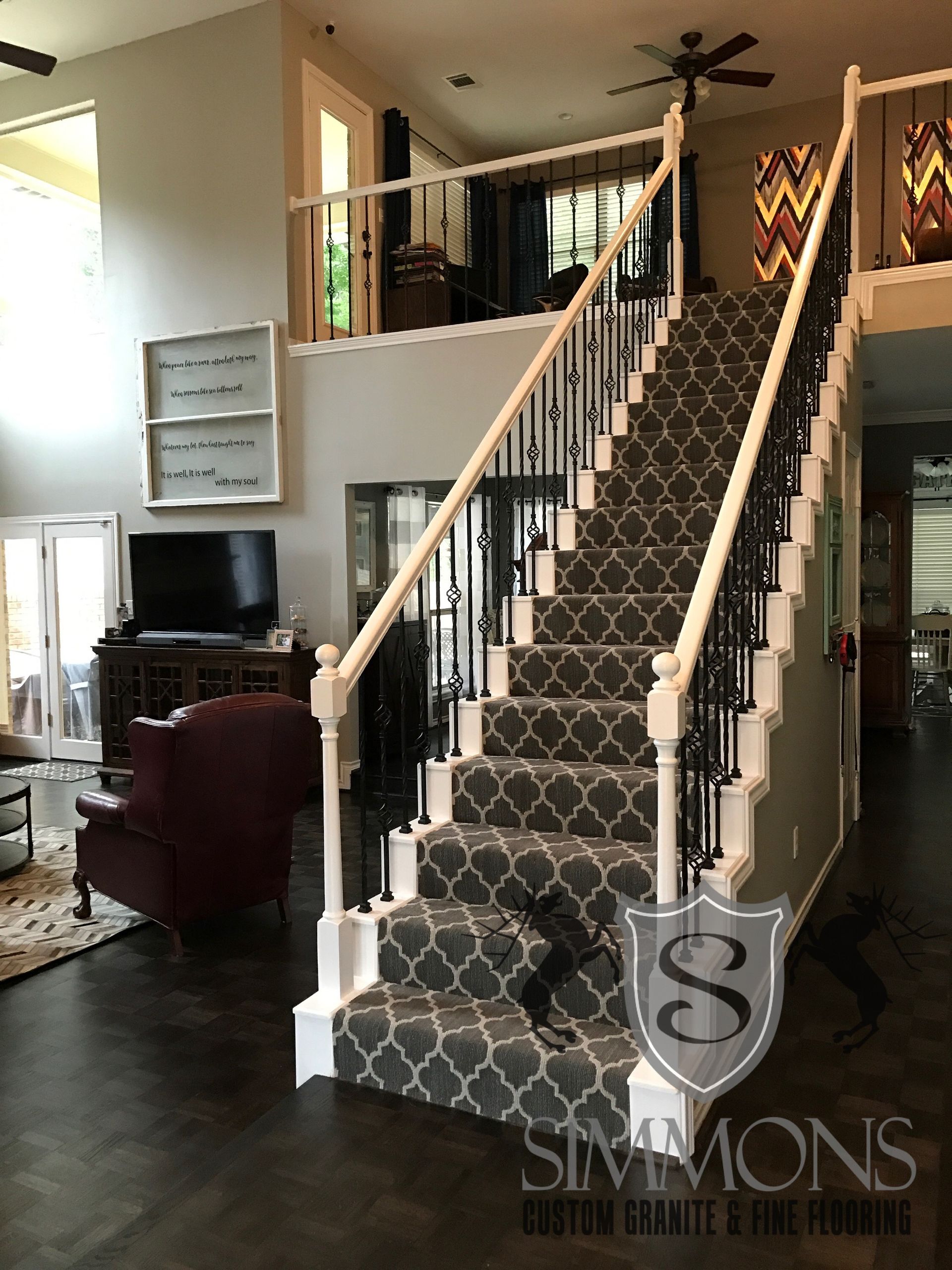 Grand staircase with patterned carpet in a lobby, topped by a railing and a ceiling fan above.