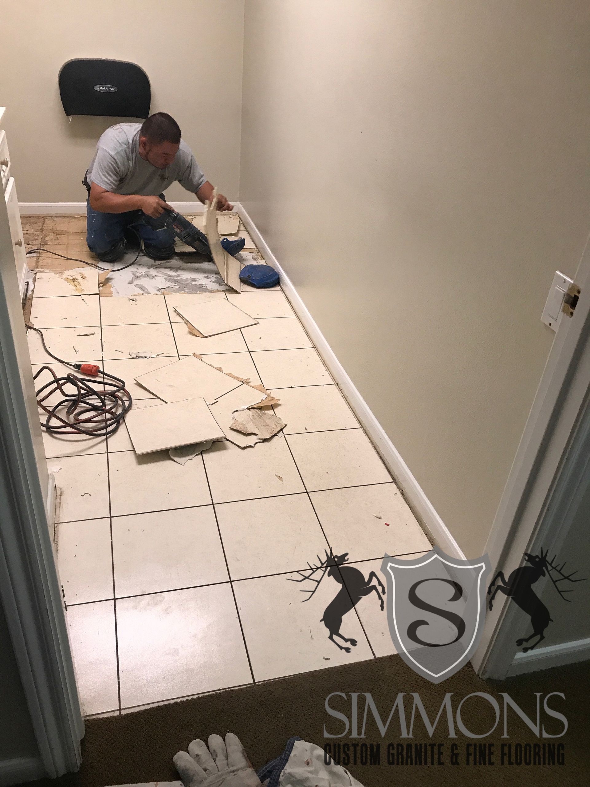 Worker installing tile floor in a hallway with tools and supplies scattered nearby.