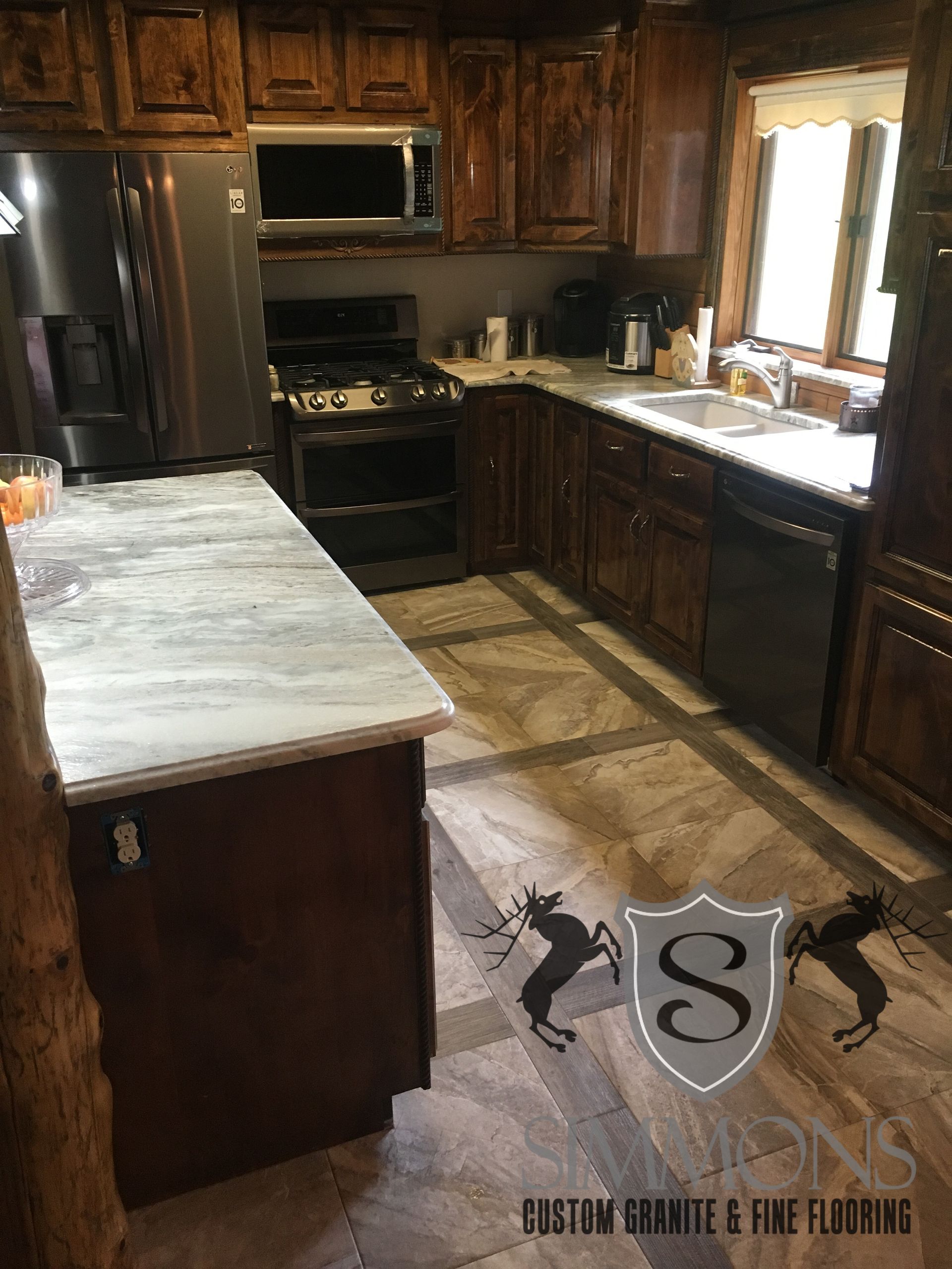Dark wood kitchen with black appliances, marble island, and sunlit window over sink.