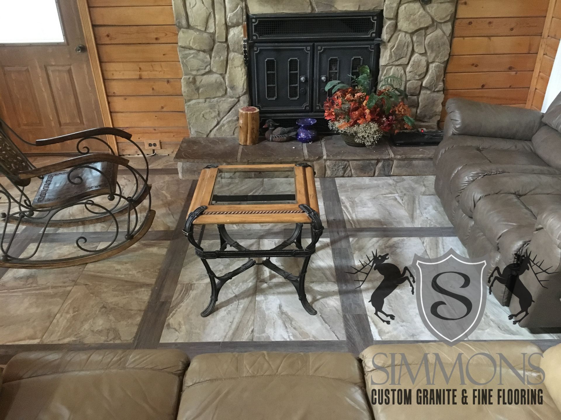 Living room with stone fireplace, gray sectional, glass coffee table, and wood-paneled walls