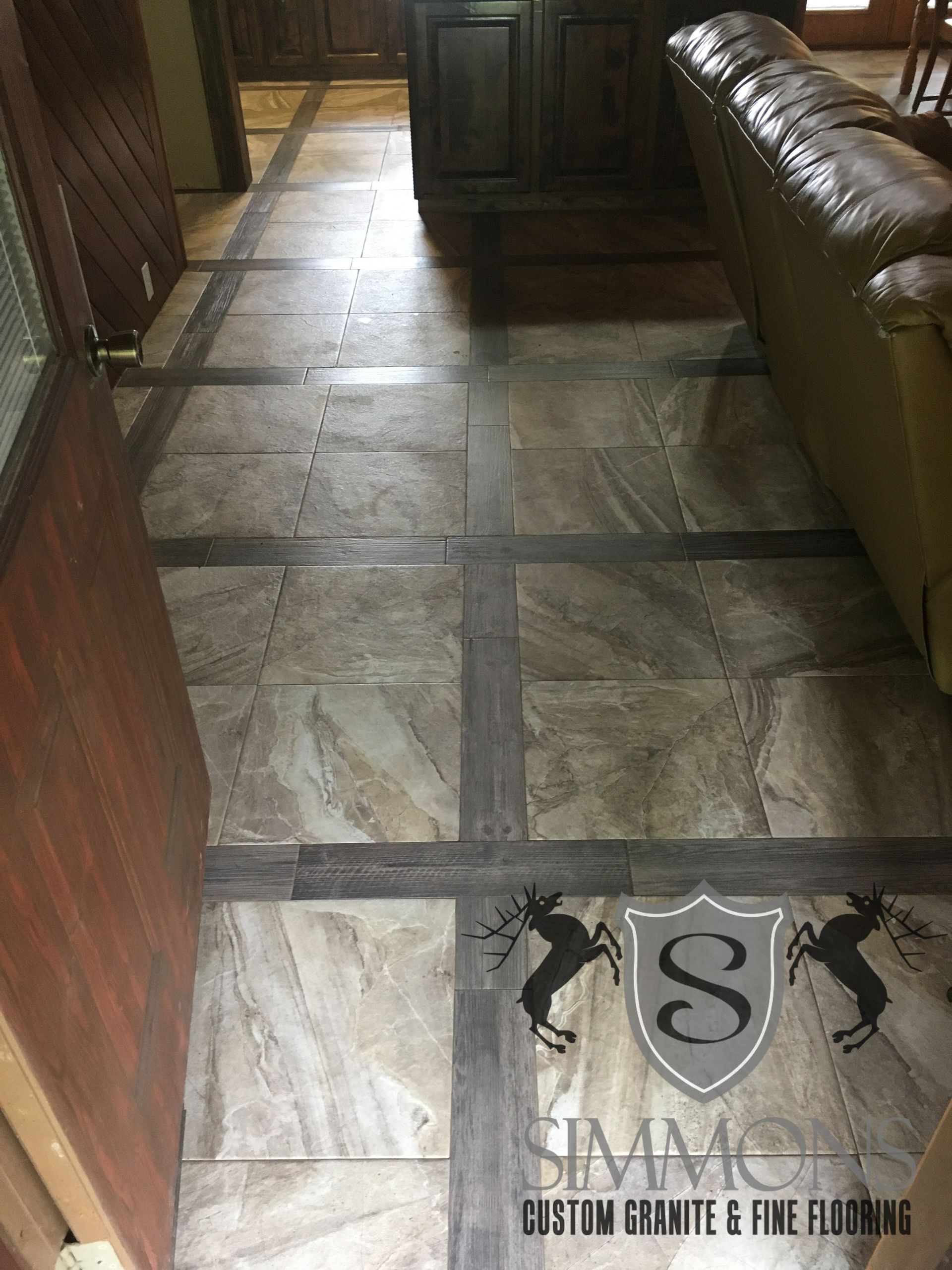Tiled hallway beside a brown leather sofa, with a cabinet in the distance and a logo watermark near the bottom.