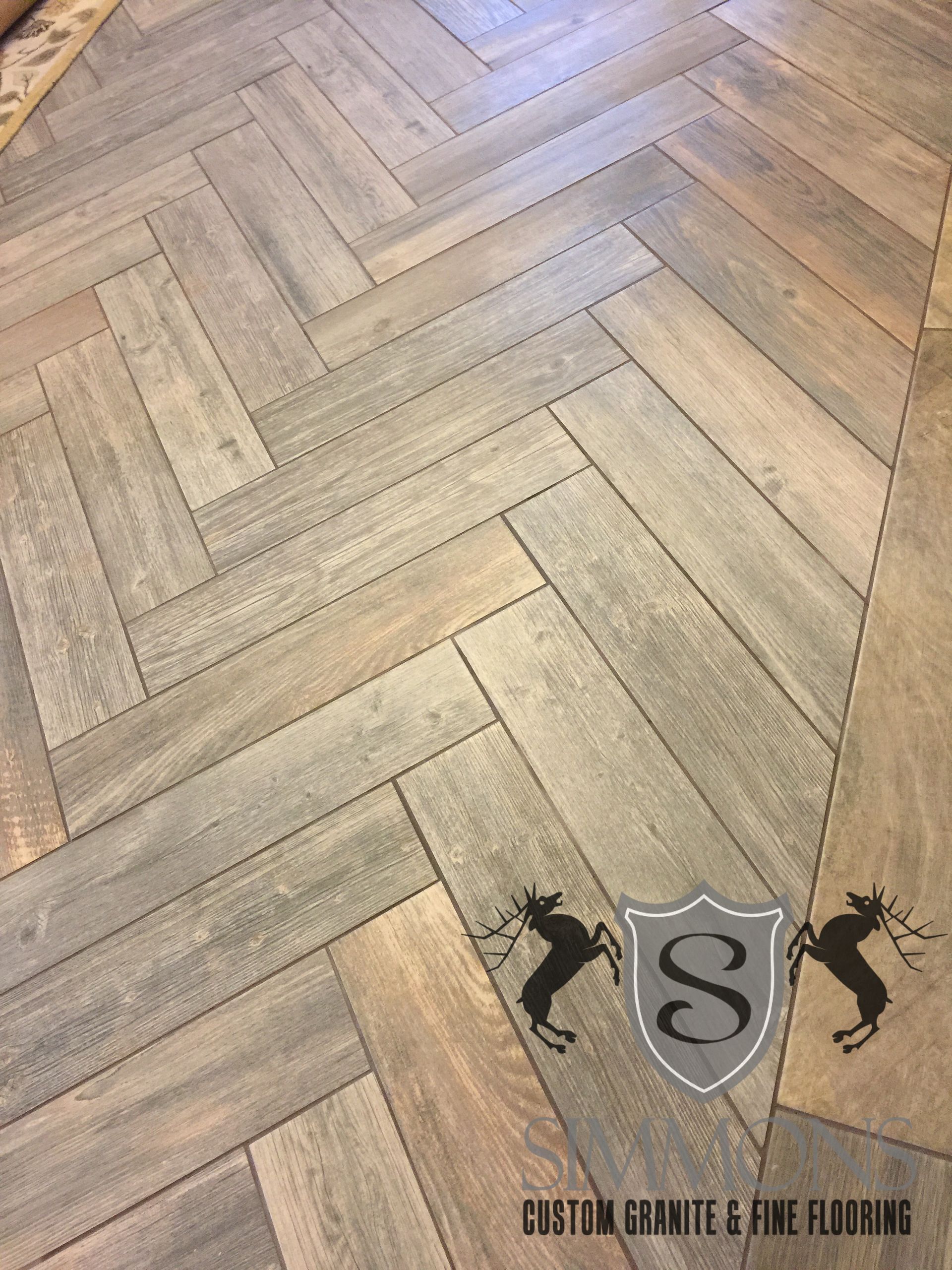 Herringbone wood floor with a small black logo and text near the bottom right.