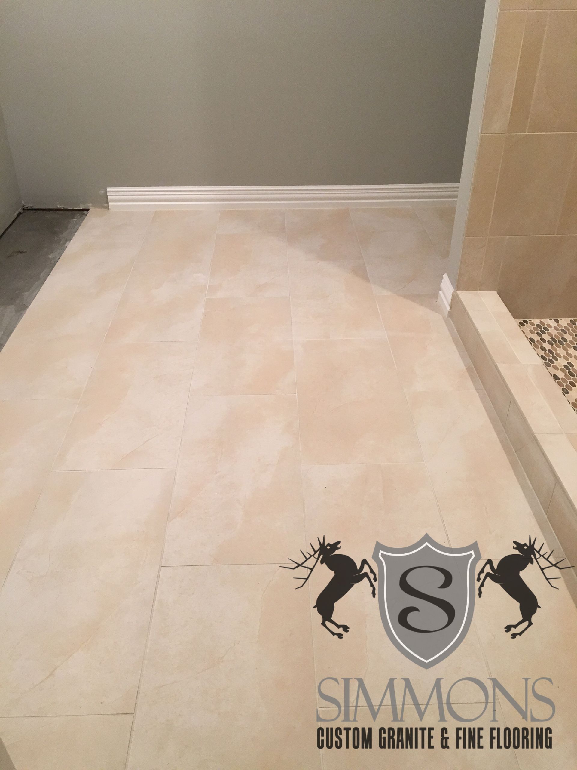 Light beige tiled floor and shower area with white baseboard trim and tan wall tiles