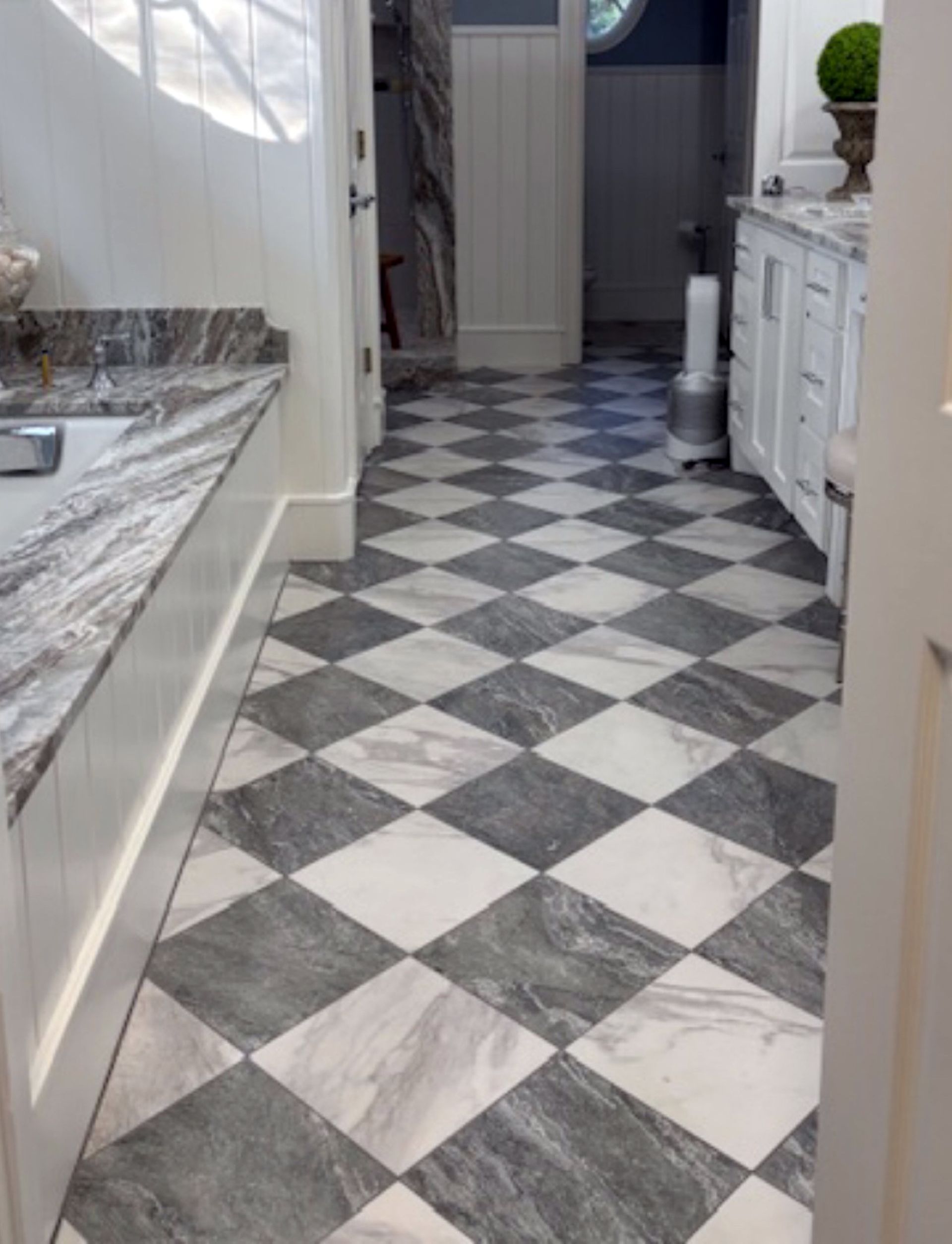 Narrow hallway with black-and-white diamond tile floor, white cabinets, and a granite countertop leading to a doorway