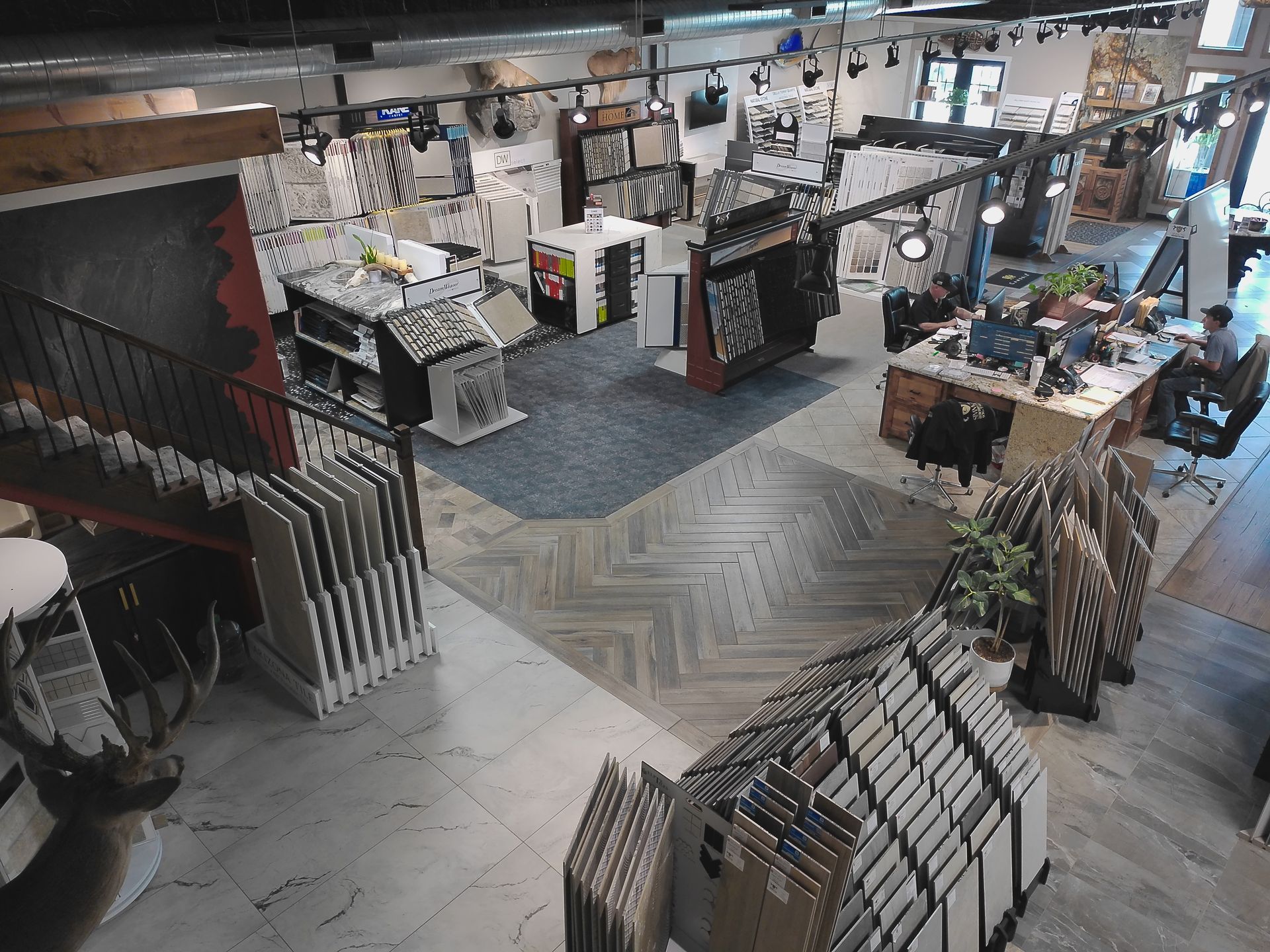 Indoor retail showroom with carpet and rug displays, shelves, and framed samples under bright lighting.