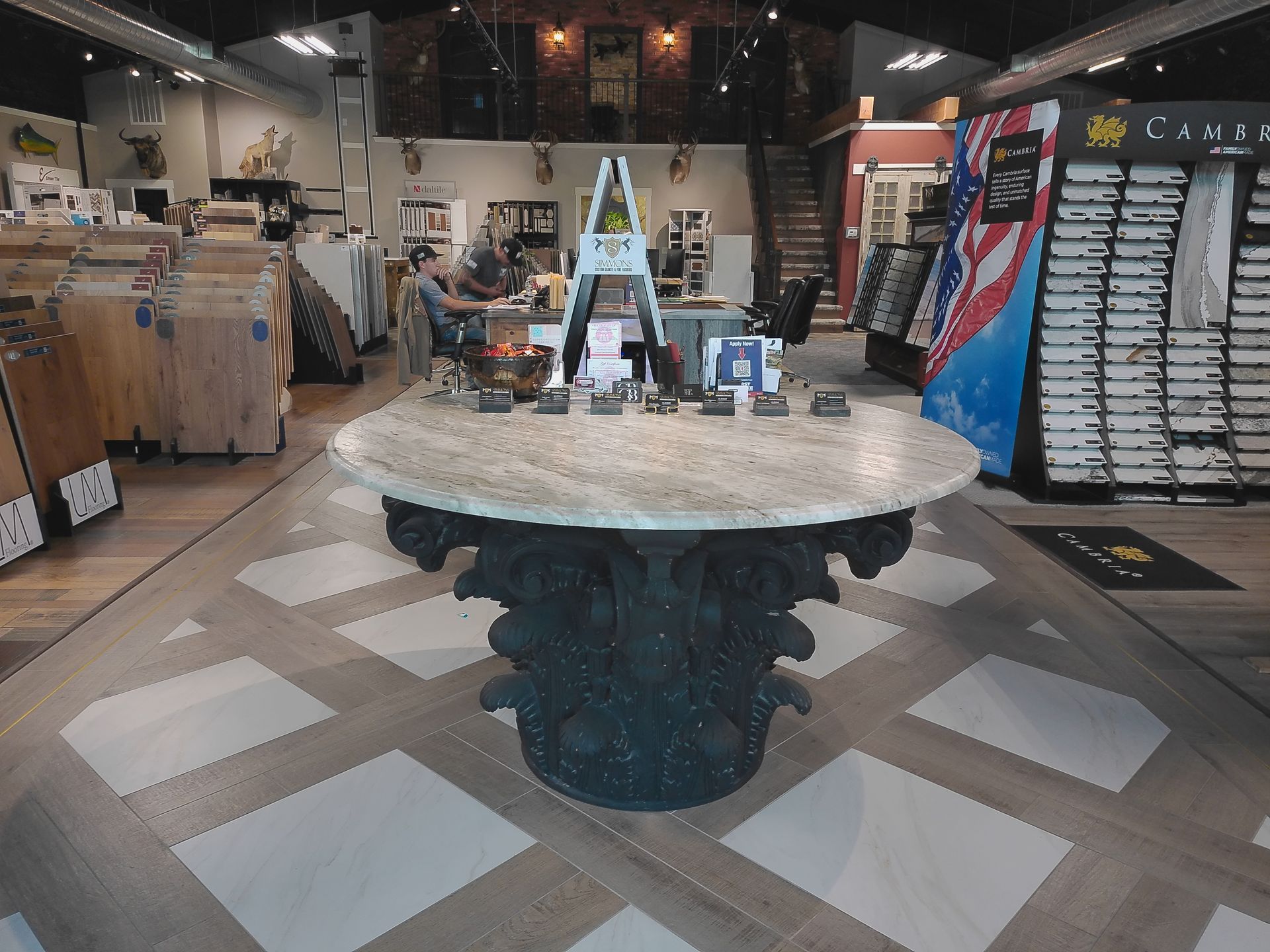 Showroom with a round stone table centered on a patterned floor, surrounded by home decor displays.