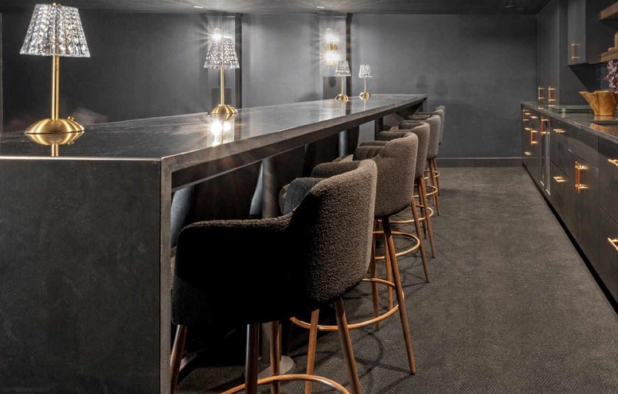 Modern bar interior with gray walls, high stools, and warm pendant lights along a dark counter.