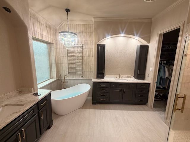 Spacious beige bathroom with freestanding tub, double vanity, and walk-in closet visible through open doorway