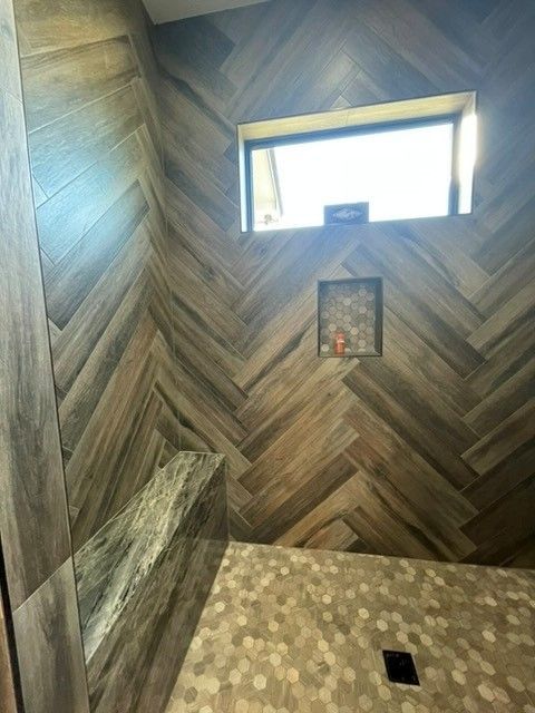 Small tiled bathroom with herringbone wood-look walls, a window, and a recessed niche above the tub.