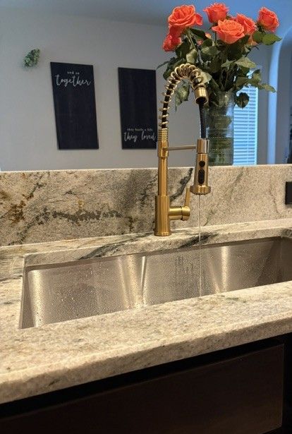 Modern kitchen sink with gold faucet, granite countertop, and red flowers in a vase on the island.