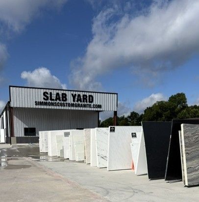 Outdoor slab yard with rows of large stone slabs in front of a warehouse under a blue sky