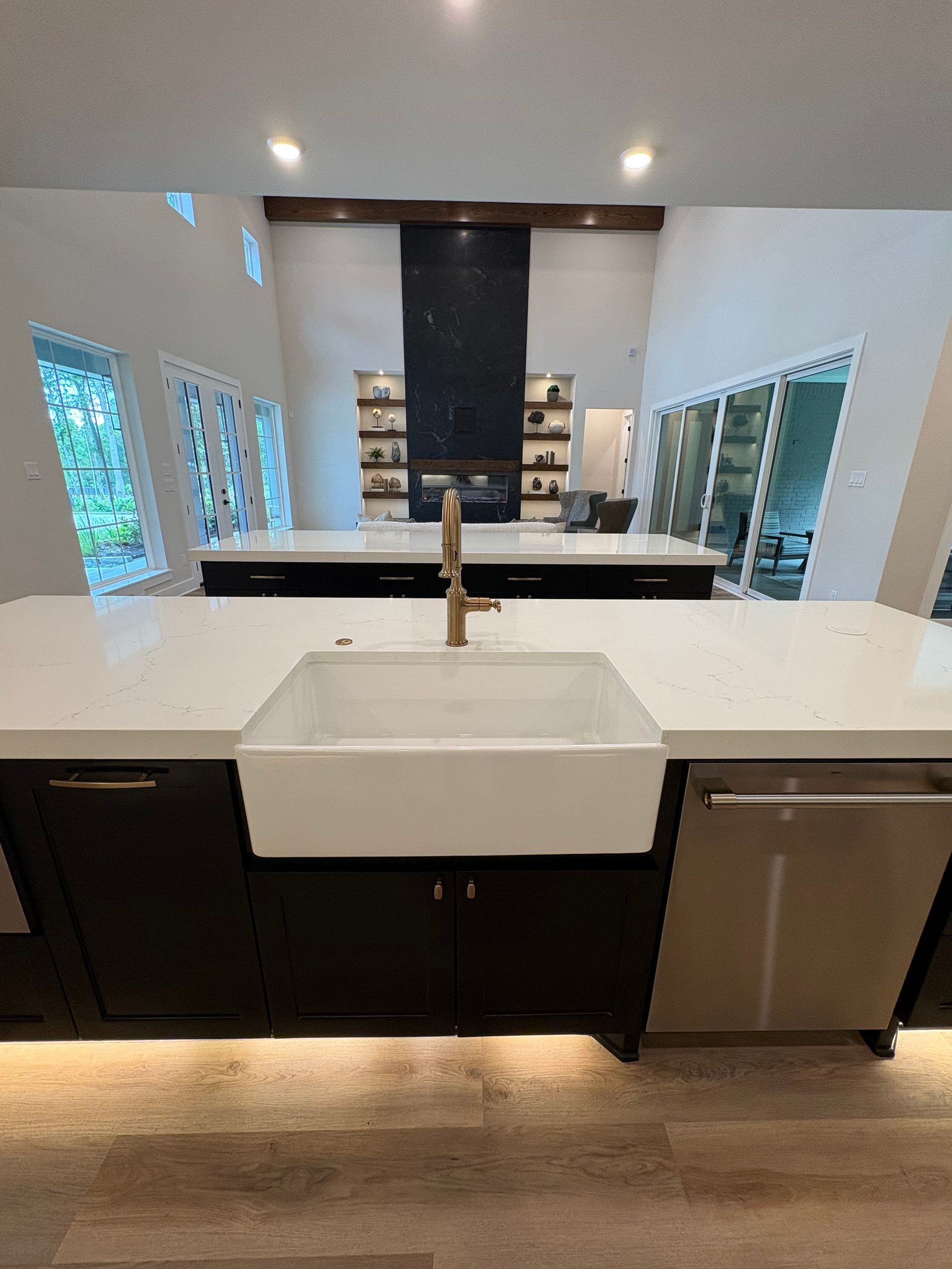 Modern kitchen with a white island, black cabinets, farmhouse sink, and pendant lighting.