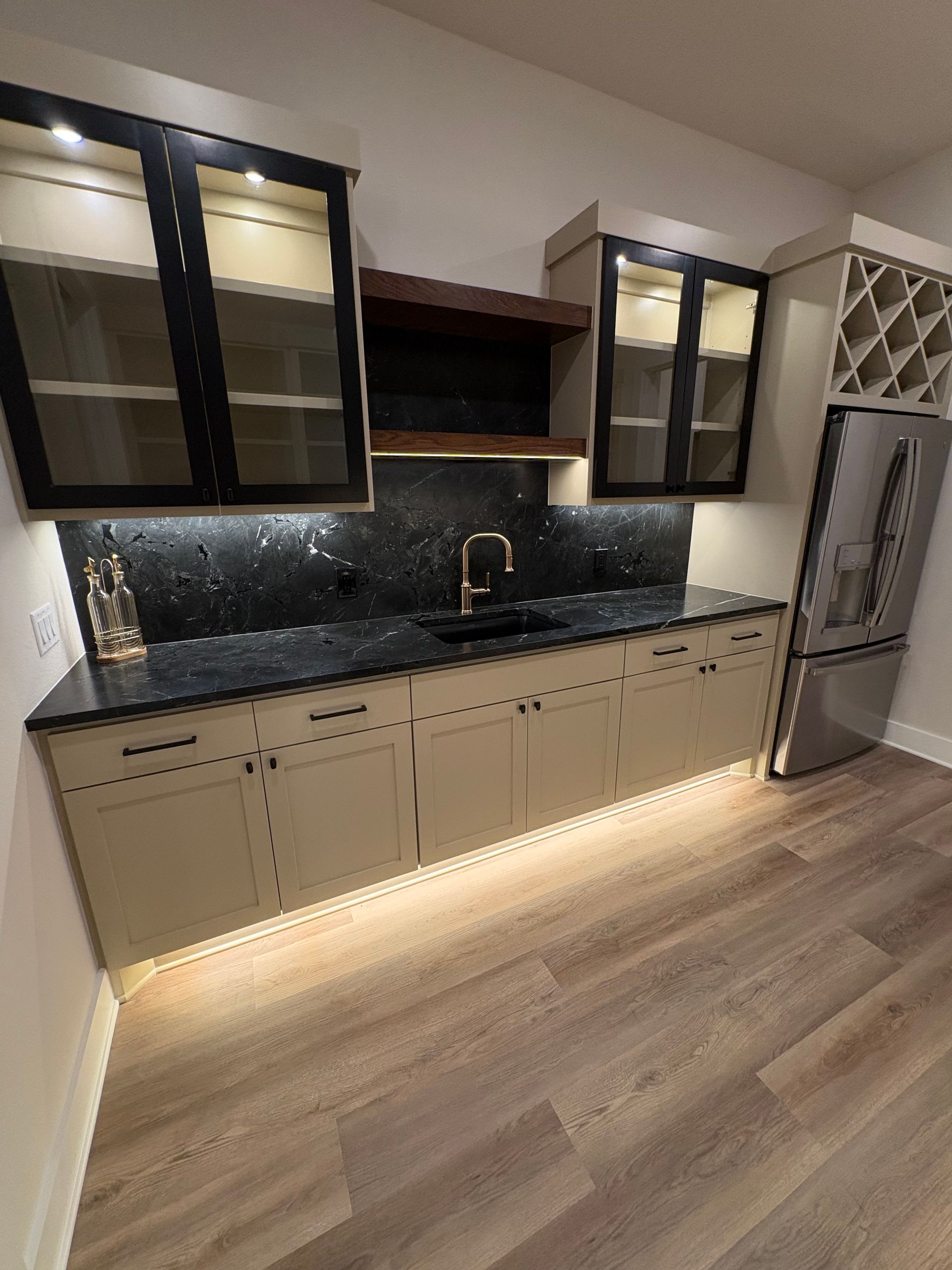 Modern kitchen with beige cabinets, dark countertop, glass-front uppers, and stainless steel refrigerator