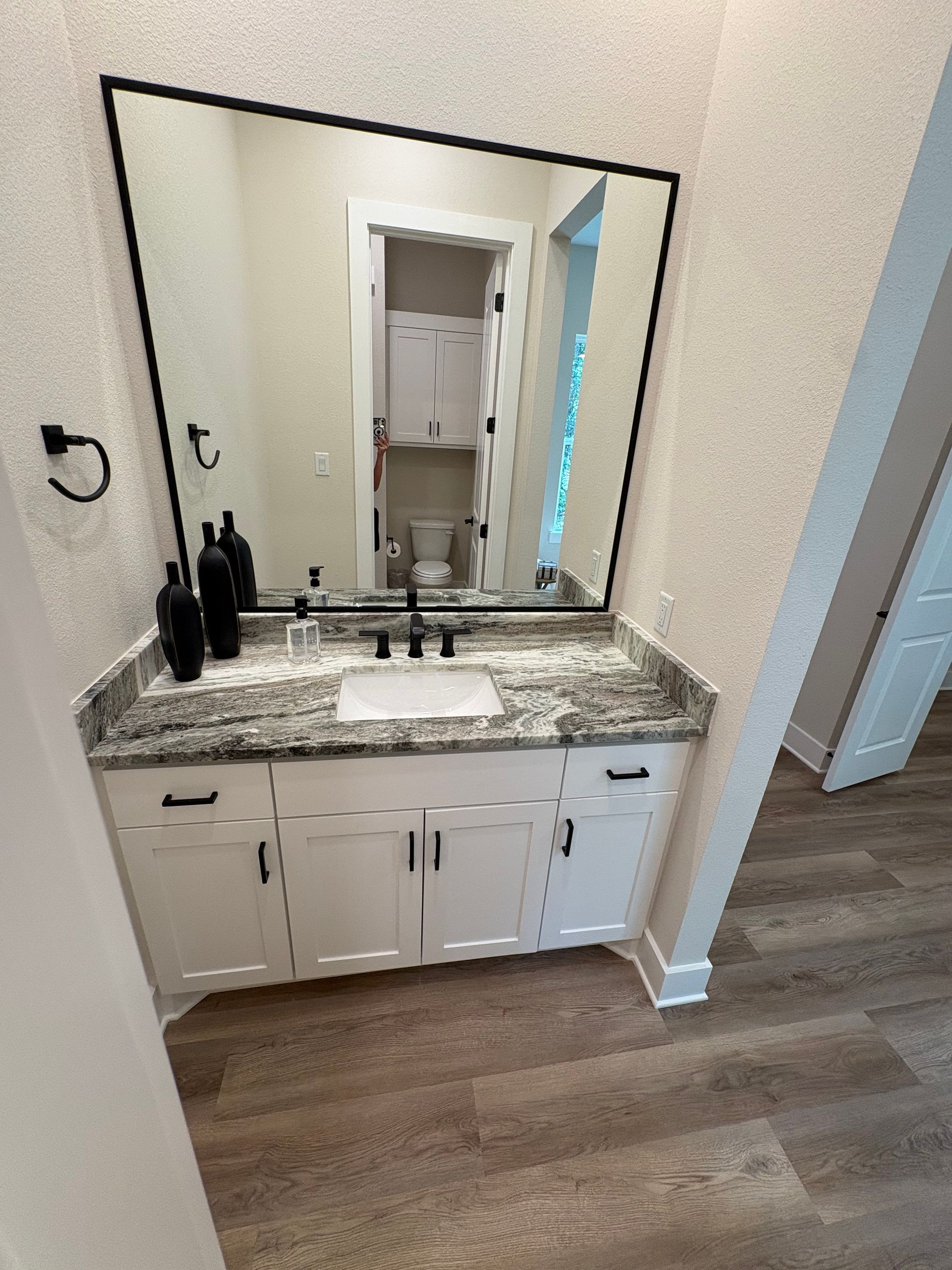 Bathroom vanity with granite countertop, large mirror, and white cabinets on wood-look flooring