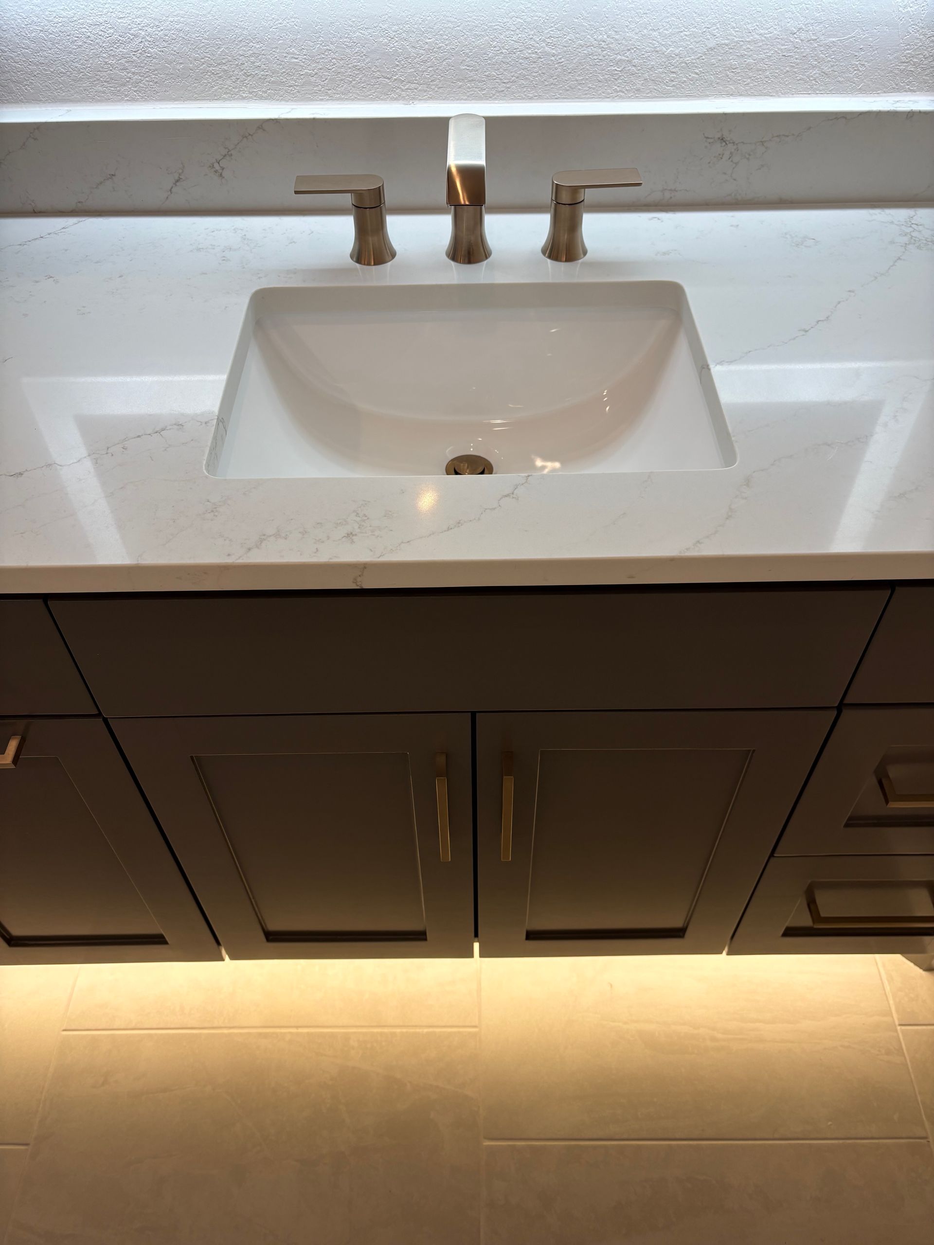 Bathroom vanity with white sink, bronze faucet, dark cabinets, and under-cabinet lighting