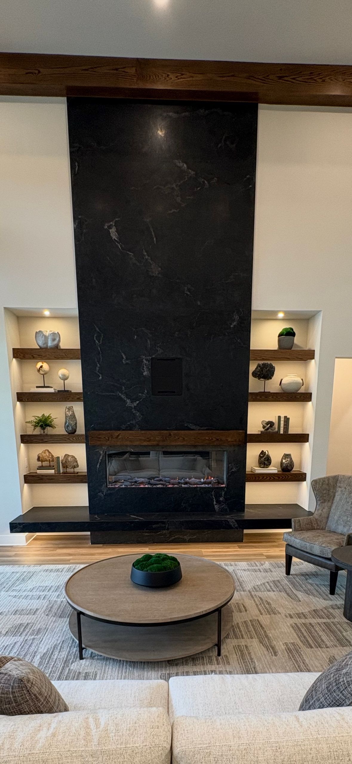 Modern living room with a tall black fireplace, built-in shelves, and a round coffee table.