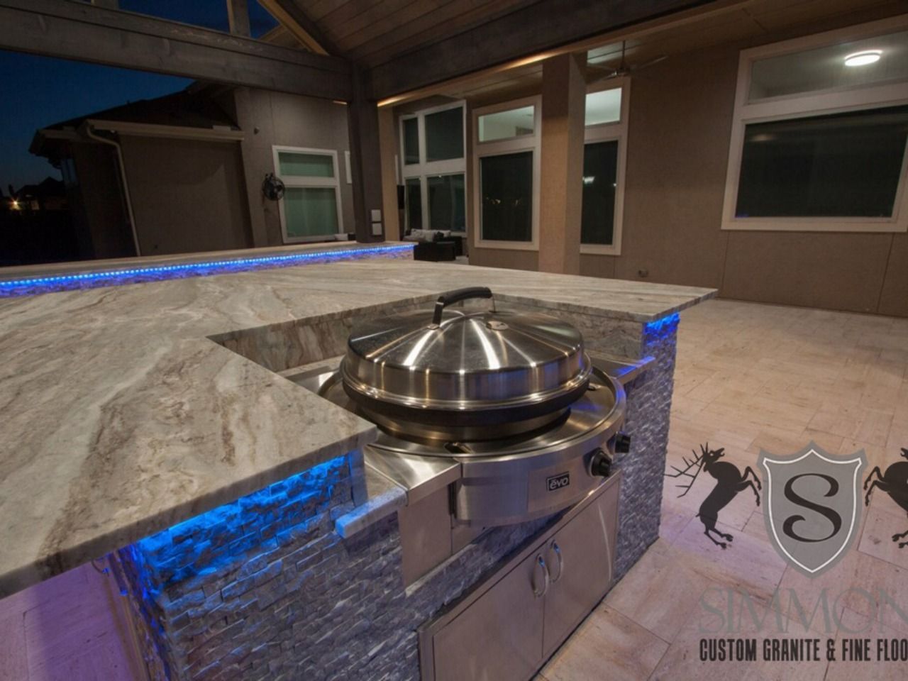 Outdoor kitchen with granite countertop, built-in grill, and blue LED accent lighting at night