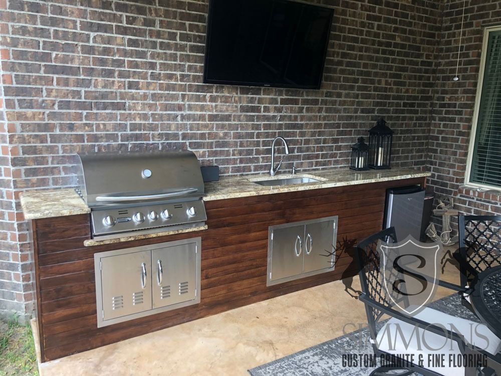 Outdoor brick patio with built-in stainless grill, sink, and cabinets under a wall-mounted TV