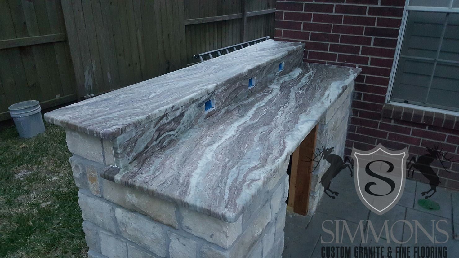 Small stone outdoor box with a weathered gray top beside a brick wall and wooden fence.