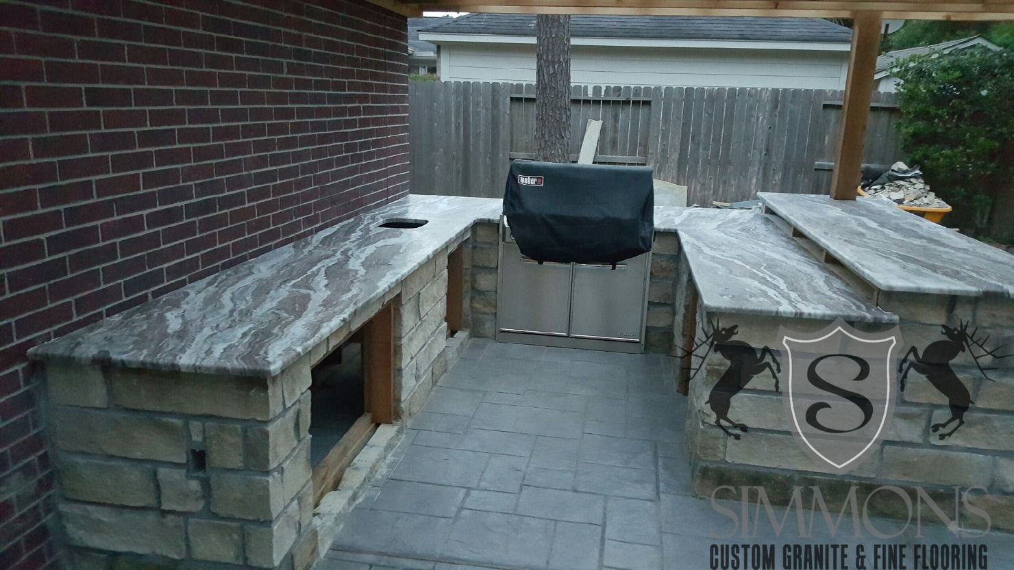 Outdoor brick patio with built-in benches, a grill, and a concrete table in a snowy yard.