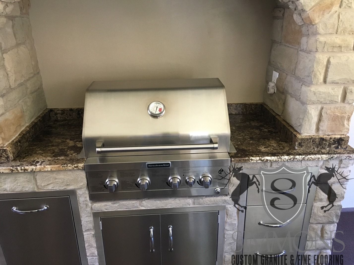 Built-in stainless steel grill with stone surround and cabinet storage underneath.