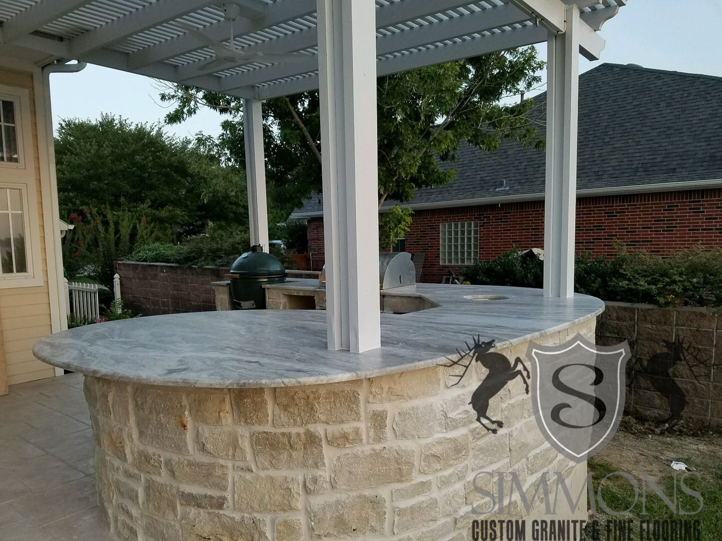 Outdoor stone gazebo with white columns and gray roof in a landscaped yard