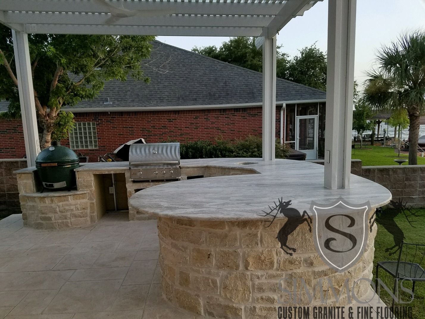 Covered patio with stone bar, grill, and outdoor seating beside a brick house