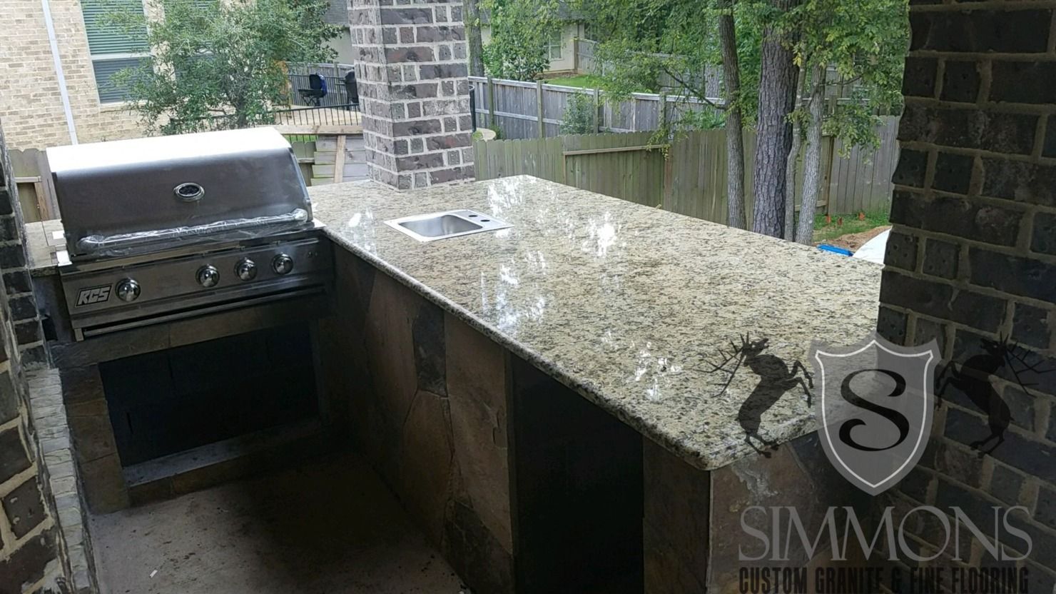 Outdoor brick patio kitchen with stainless grill and granite countertop under a covered area.