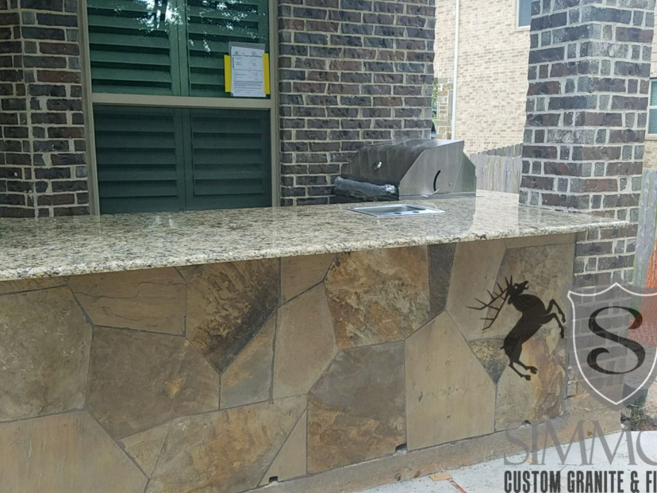 Stone countertop in a brick alcove with a small fountain spout and a black lizard decal on the wall.