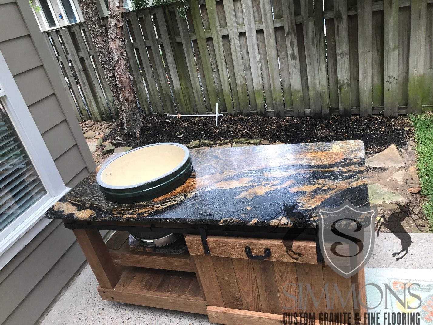 Backyard deck with a dark workbench, shallow bowl, and a black granite countertop beside a fence.