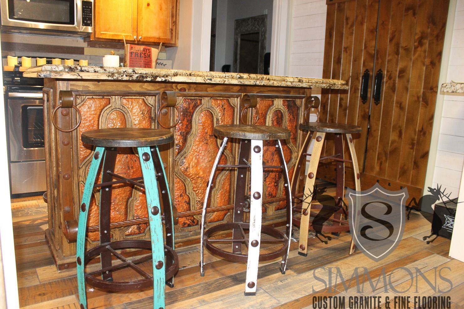 Kitchen island with granite countertop and three metal bar stools in a warm wood kitchen
