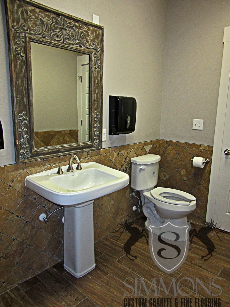 Small bathroom with pedestal sink, toilet, ornate mirror, and brown tile walls.