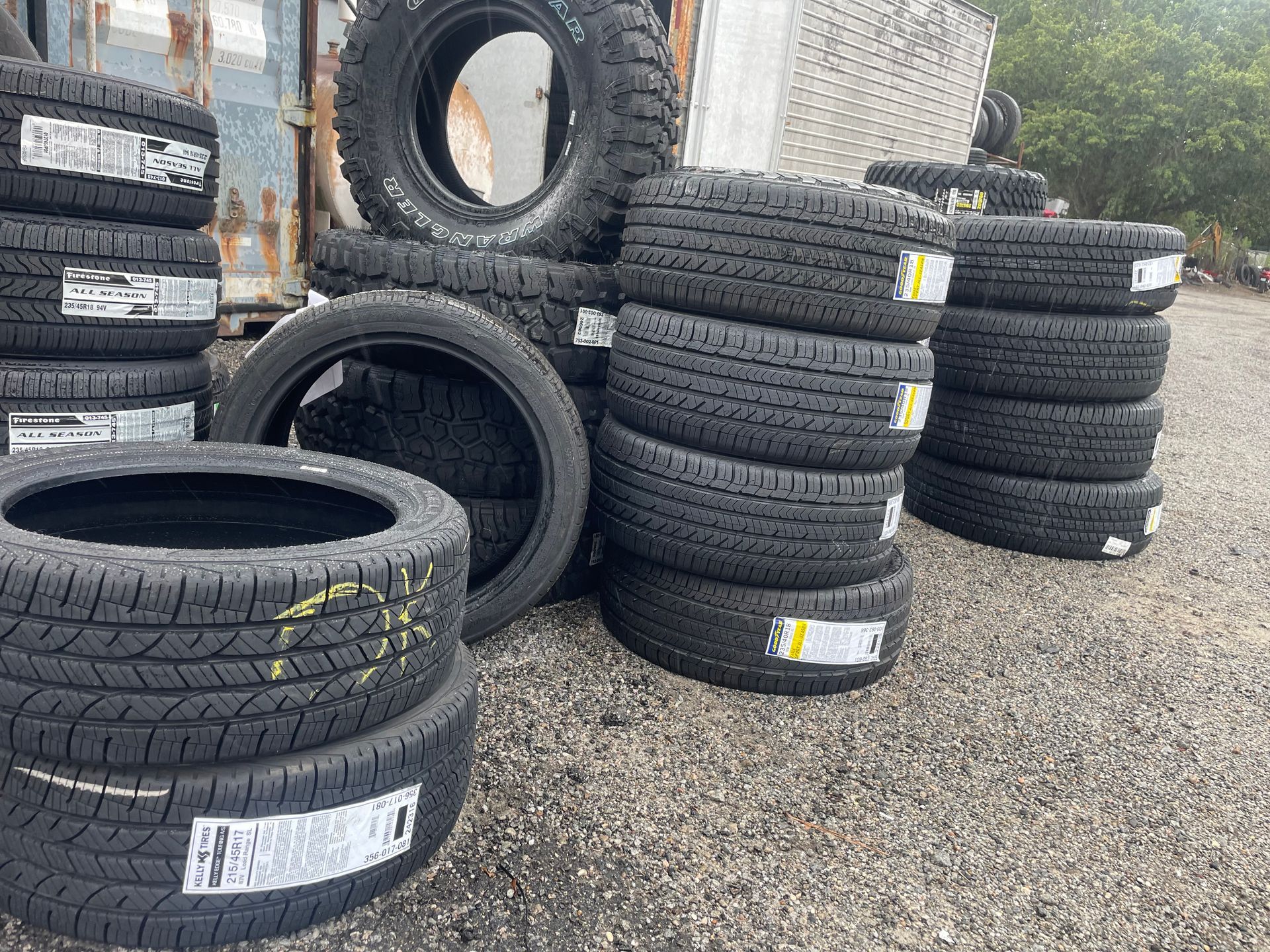 Piles of new black tires stacked outdoors, some with labels, near a metal container.