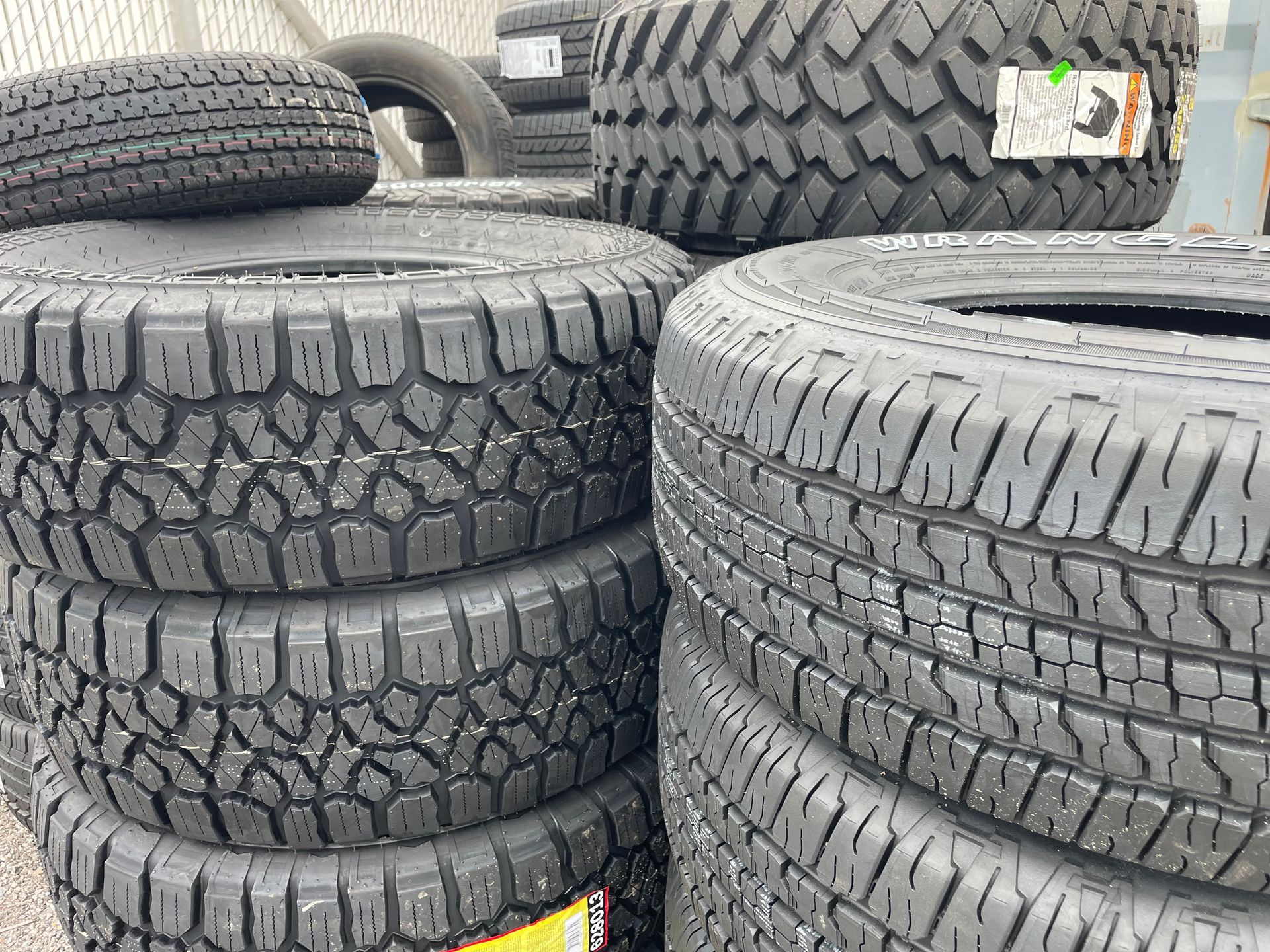 Stacks of new black tires with tread patterns, possibly for off-road vehicles, in a store or warehouse.
