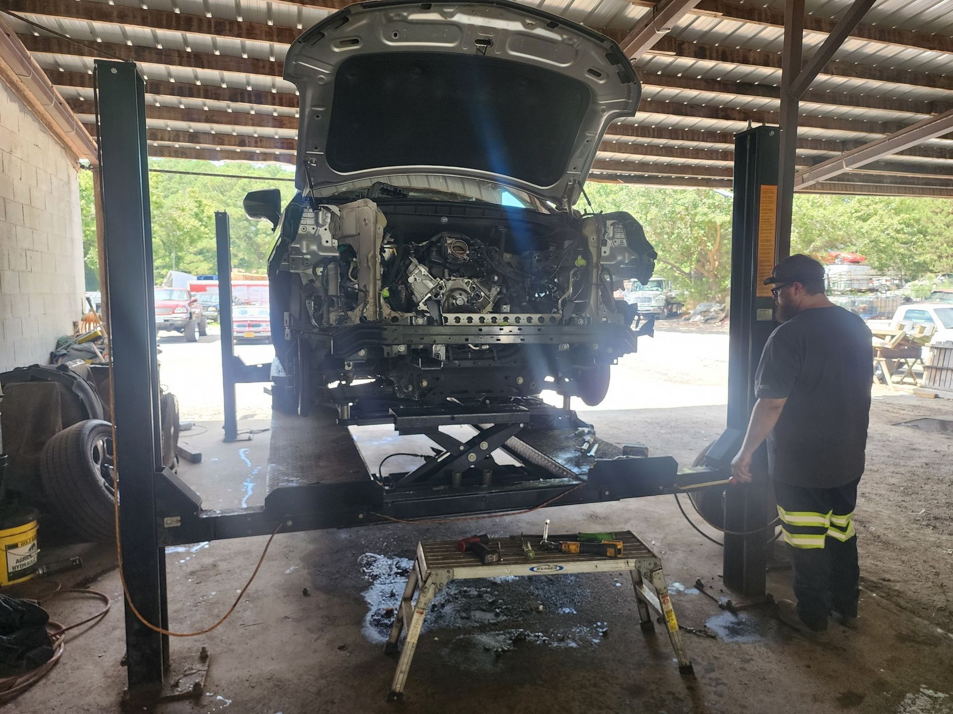 A damaged car on a lift in a repair shop, worker adjusting lift.