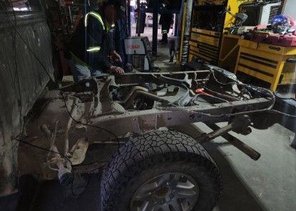 Man working on a truck frame in a workshop, with tools and a tire visible.
