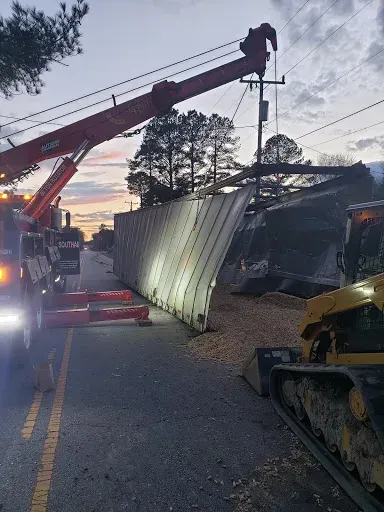 A tow truck and bulldozer removing a damaged metal structure from a road. Dusk sky.