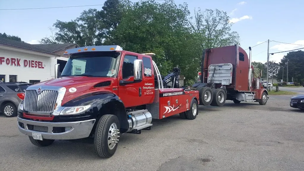 Red tow truck towing a brown semi-truck on a paved lot; 