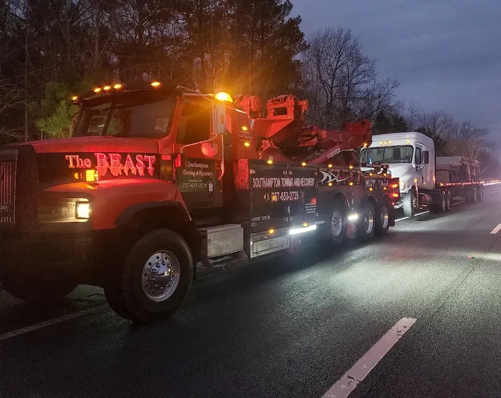 Red tow truck towing a white RV at night with flashing lights on the road.