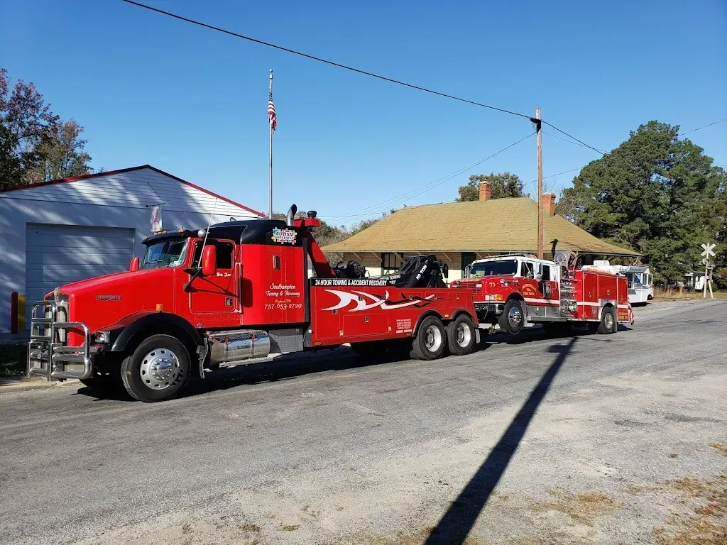 Red tow truck towing a vehicle on a trailer in front of a building on a sunny day.