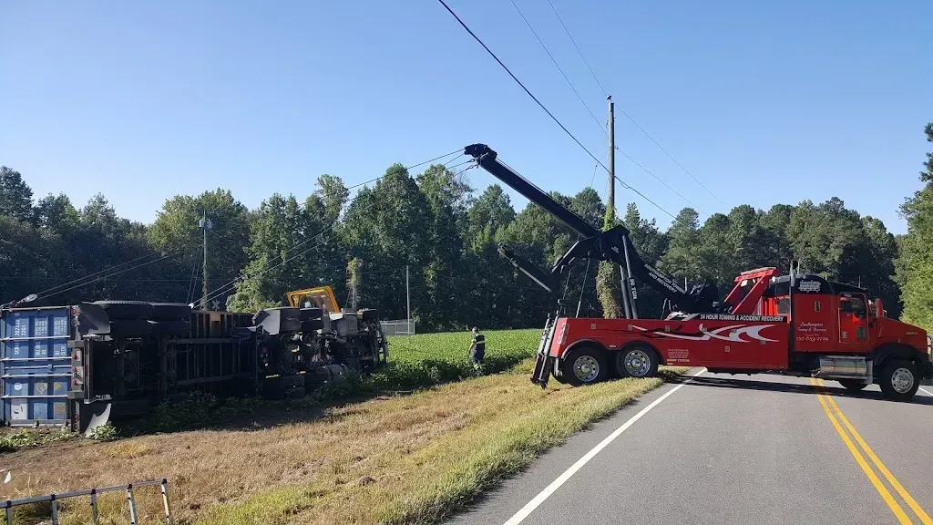 Tow truck uprighting a semi-truck that has overturned near a field, power lines overhead.