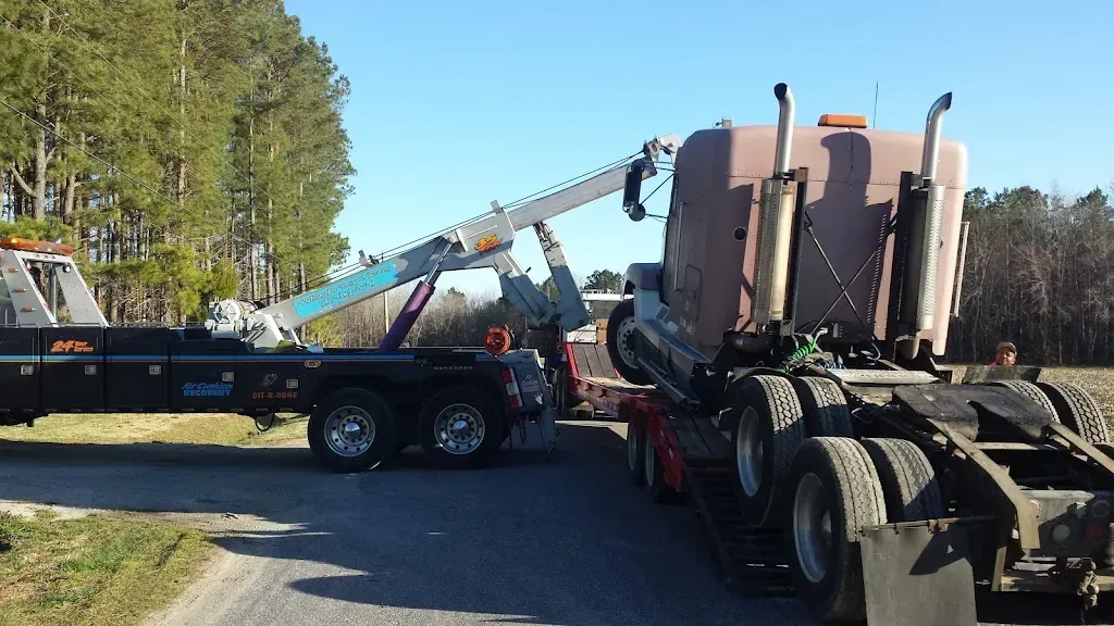 Tow truck lifting a semi-truck cab on a road. The sky is blue and trees are in the background.