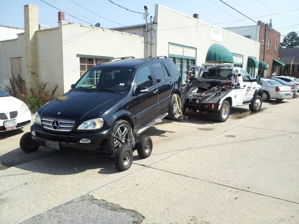 Black SUV being towed by a tow truck; the SUV's wheels are on dollies.