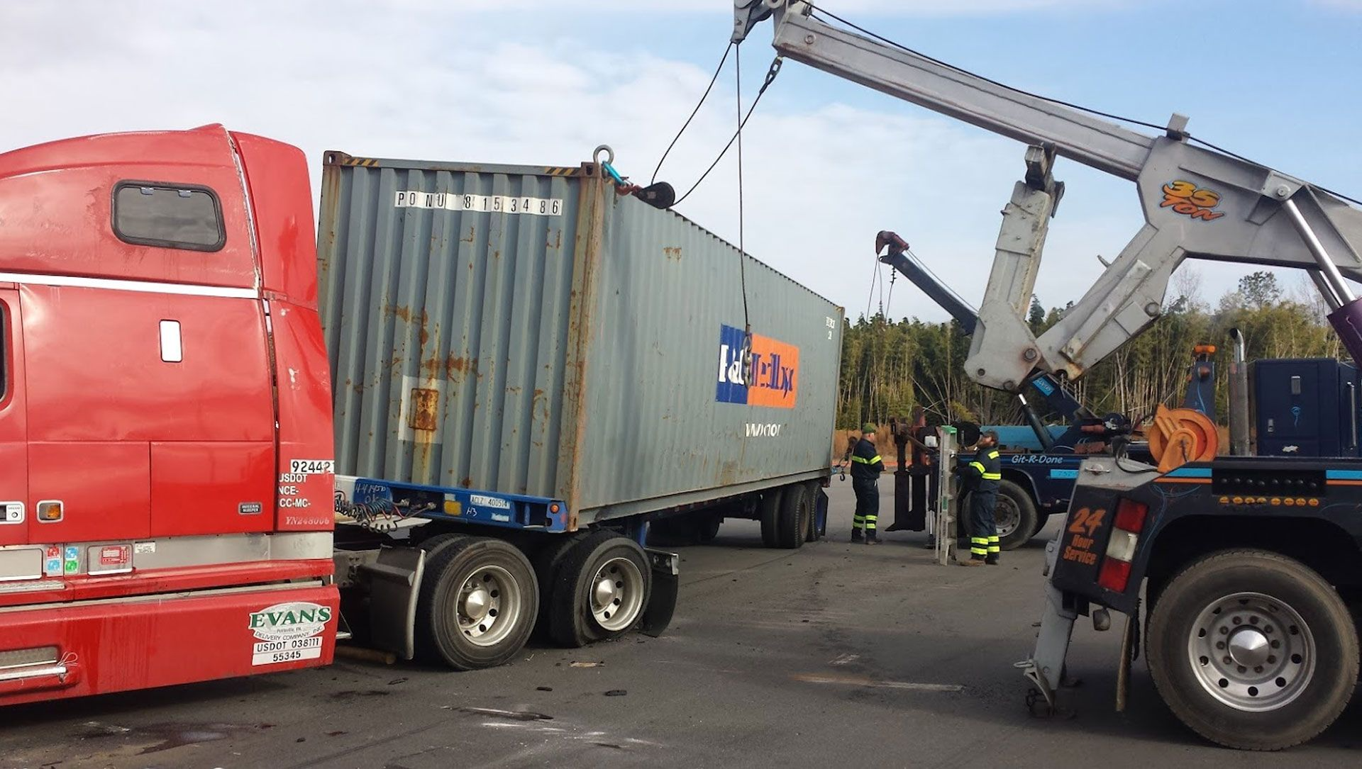 A semi-truck with a container being lifted by a crane after an accident. Emergency personnel are present.