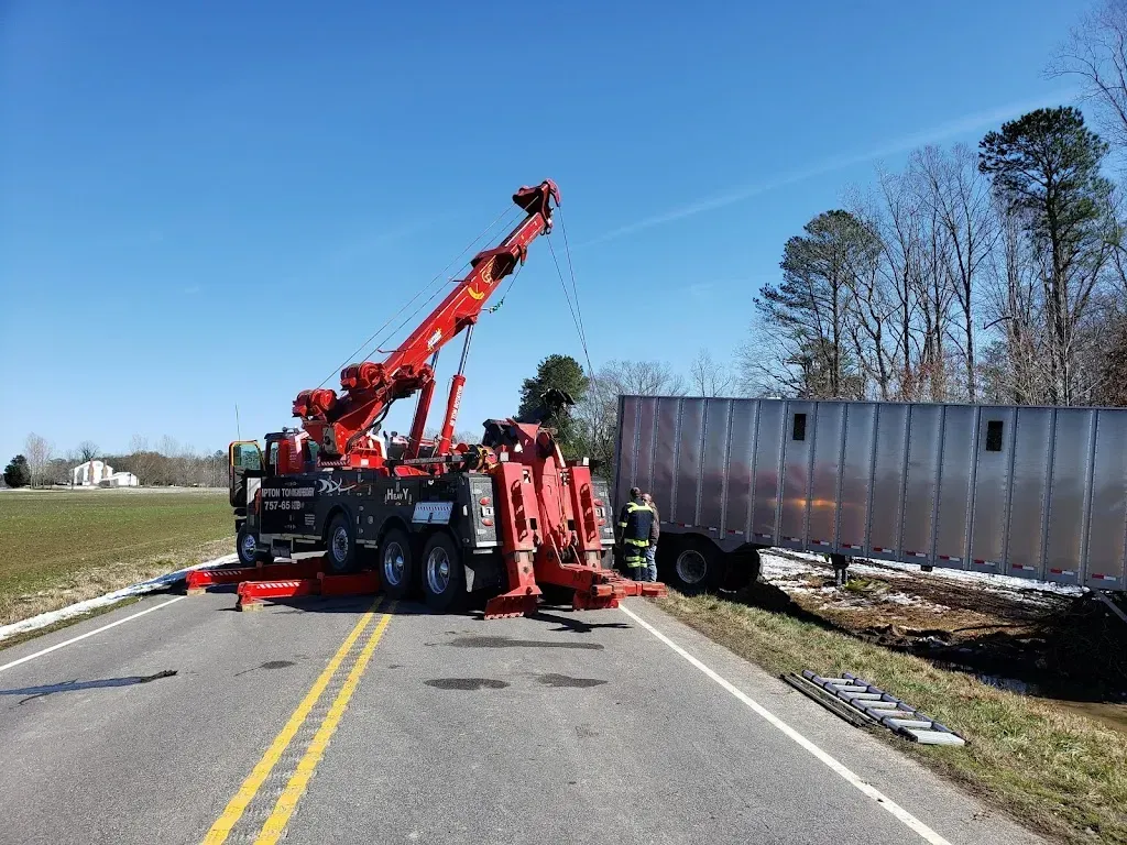 Tow truck lifting a semi-trailer out of a ditch on a road under a blue sky.